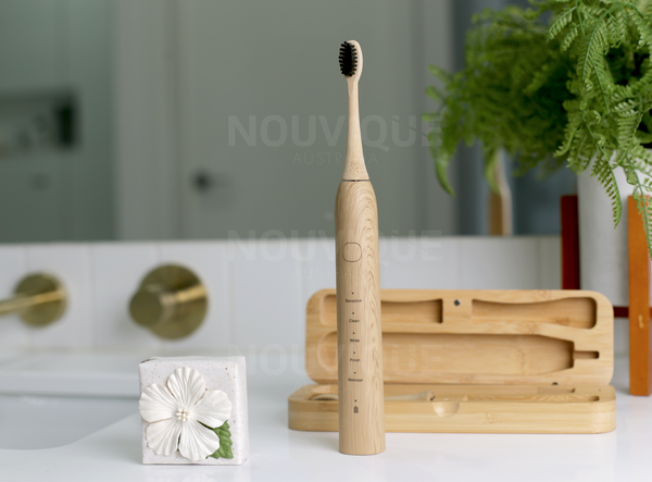 An eco electric toothbrush and bamboo travel case in a real setting next to the bathroom sink and gold taps