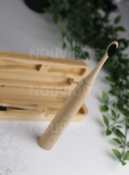 bamboo electric toothbrush is standing upright on a marble counter in front of the bamboo travel case which has a spare toothbrush head bristle